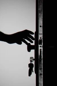 Silhouette of a hand reaching for a door knob. Door has keys hanging out of the lock