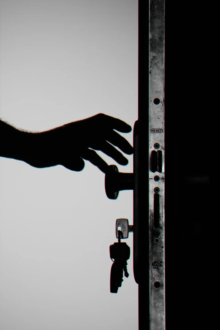 Silhouette of a hand reaching for a door knob. Door has keys hanging out of the lock