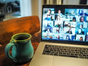 Laptop screen showing a video conference call, next to a cup of coffee on the desk